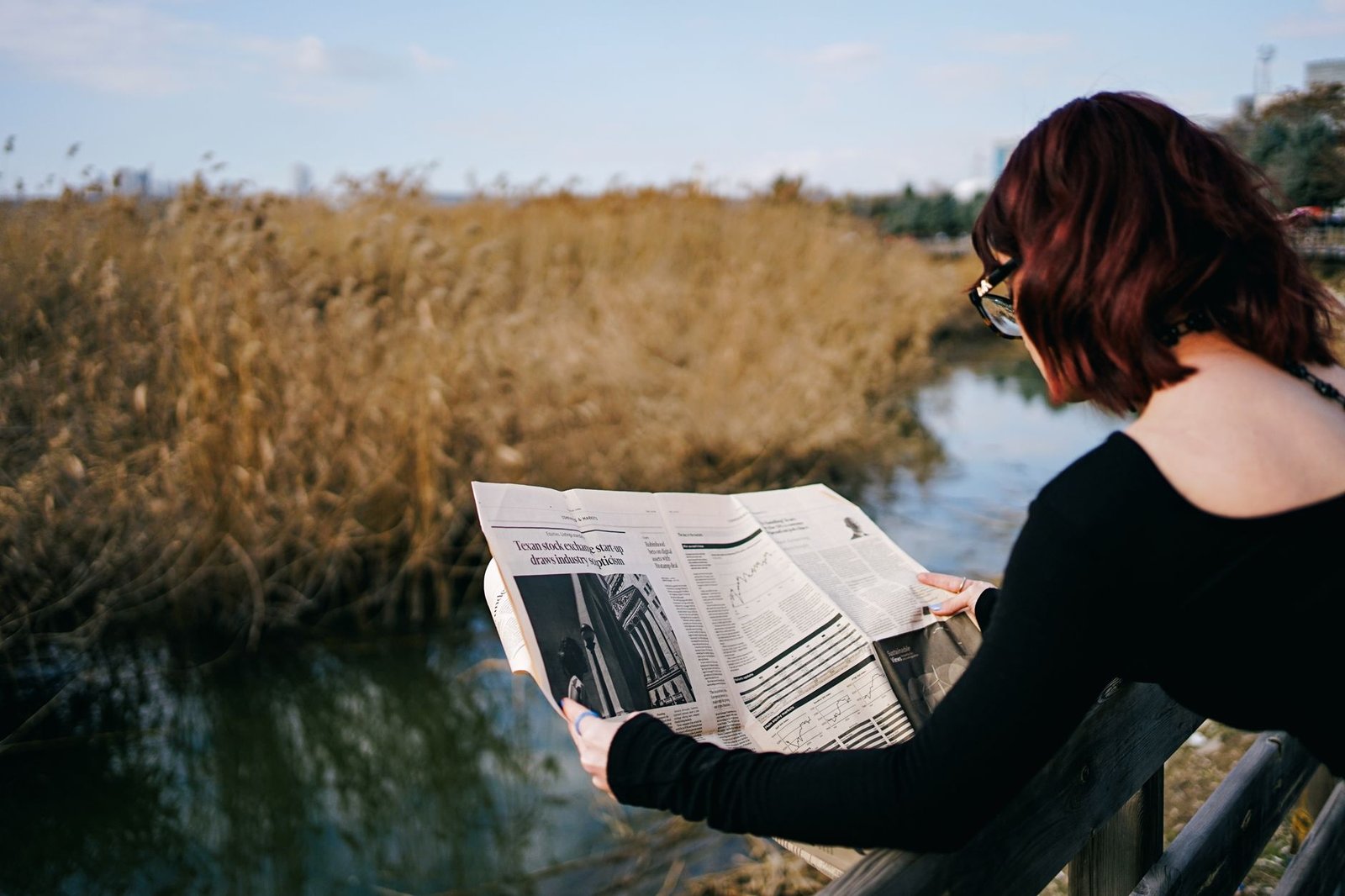 A woman reads a newspaper by a river, surrounded by autumn reeds and tranquil scenery. — Crypto casino crash game