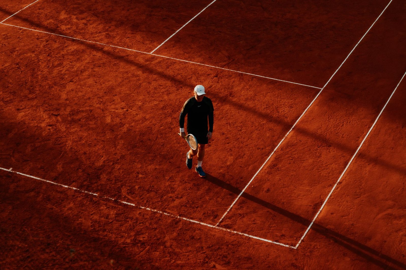 An overhead shot of a tennis player on a clay court during the day, with long shadows. — La Grada Online: The Most Reliable S